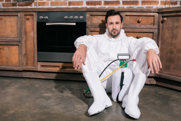 tired pest control worker sitting on floor in kitchen and looking at camera